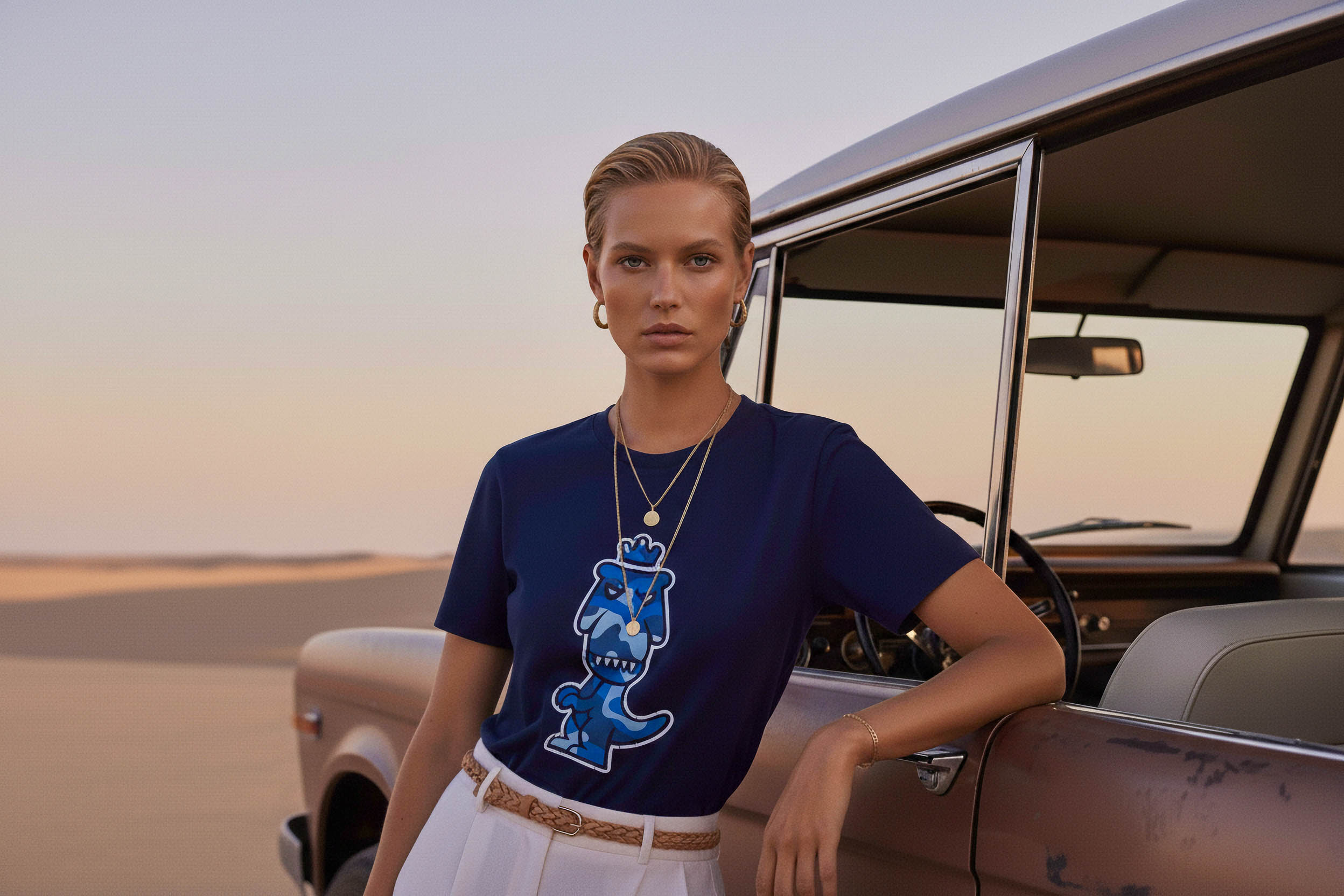 Woman wearing a navy blue Regno pima cotton graphic tee with blue T-Rex design, styled with gold jewelry and white pants, luxury streetwear aesthetic