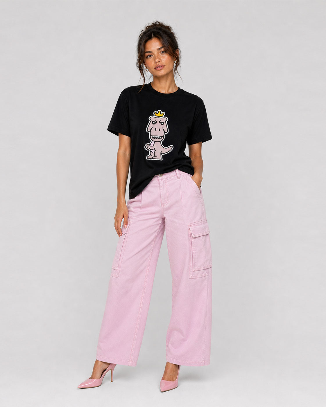 Woman wearing black Regno Nudus pima cotton luxury tee with pastel T-Rex graphic styled with pink wide leg cargo pants and heels, editorial streetwear female outfit