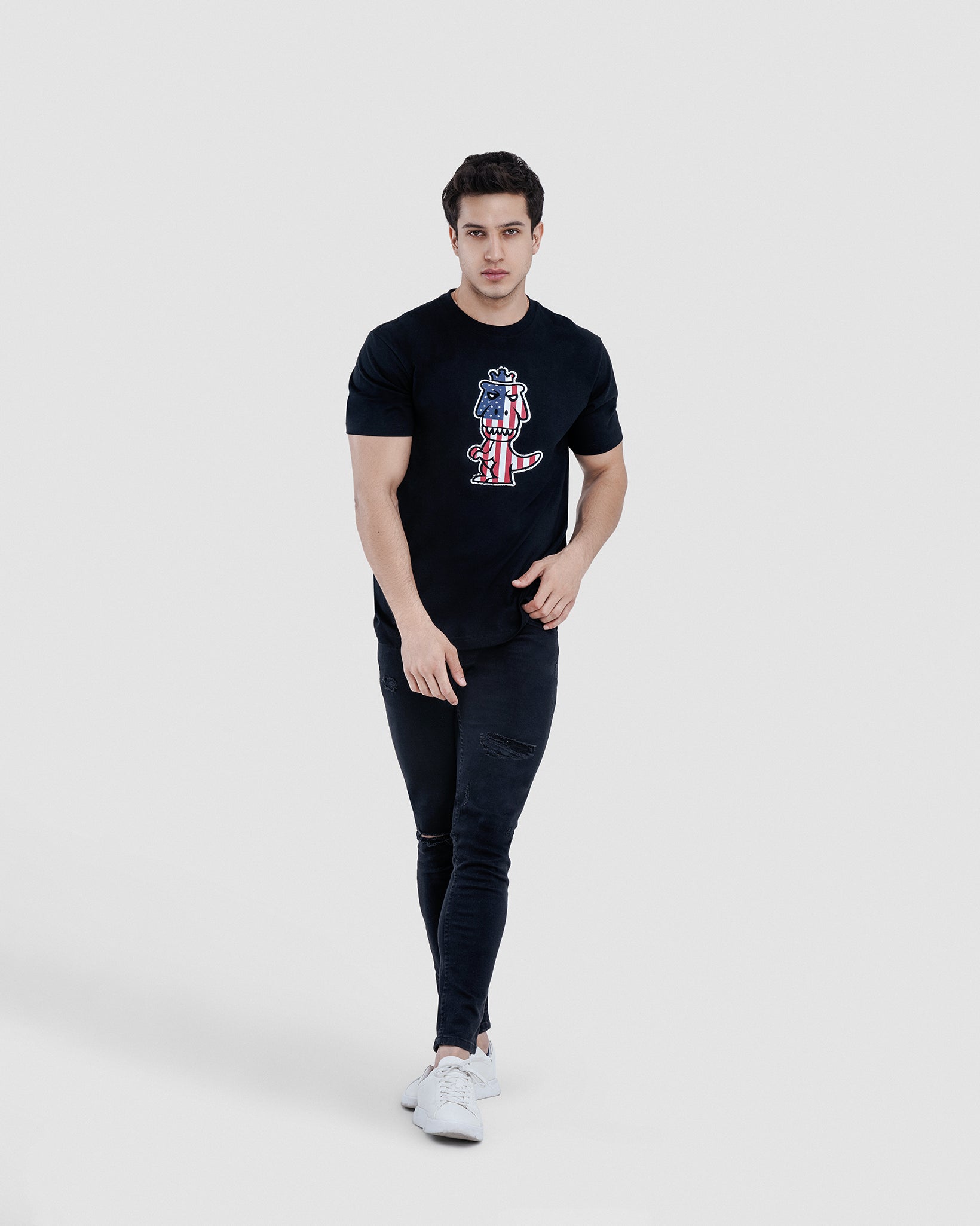 Man wearing black Reino T-Rex Libertatem pima cotton t-shirt with American flag T-Rex graphic, full body lifestyle shot